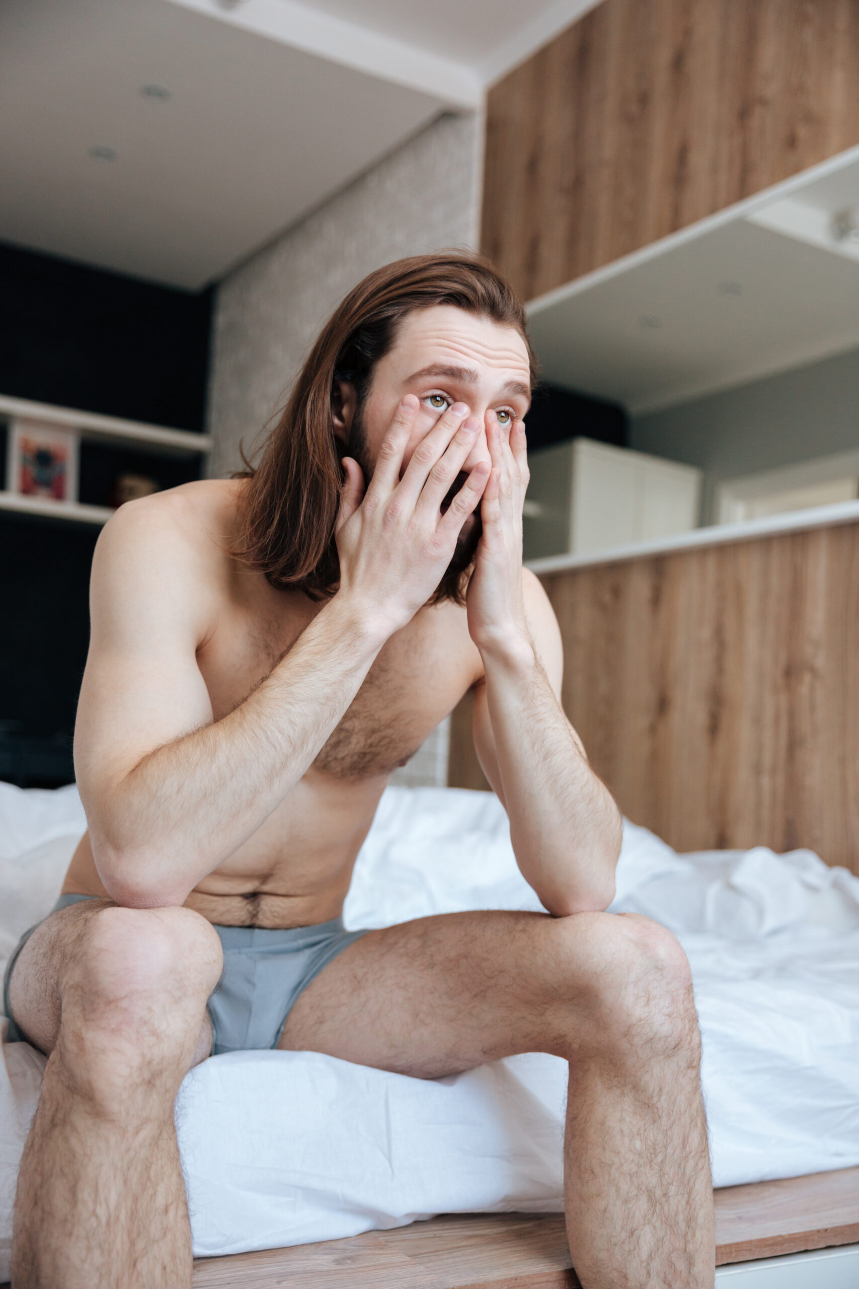Sad sleepy young man sitting on bed in the morning