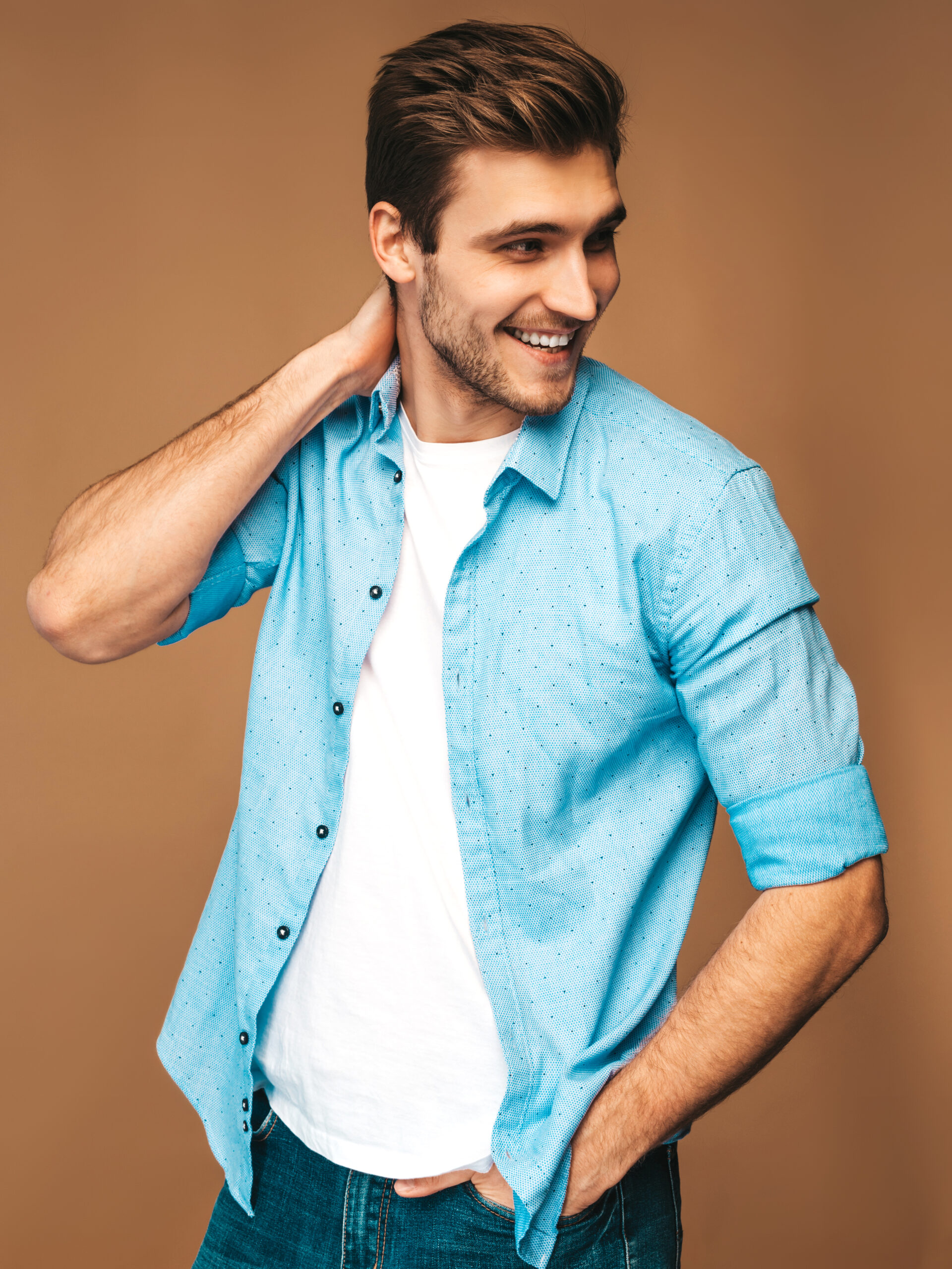 Portrait of handsome smiling stylish hipster lumbersexual businessman model dressed in blue shirt clothes. Fashion man posing on golden background